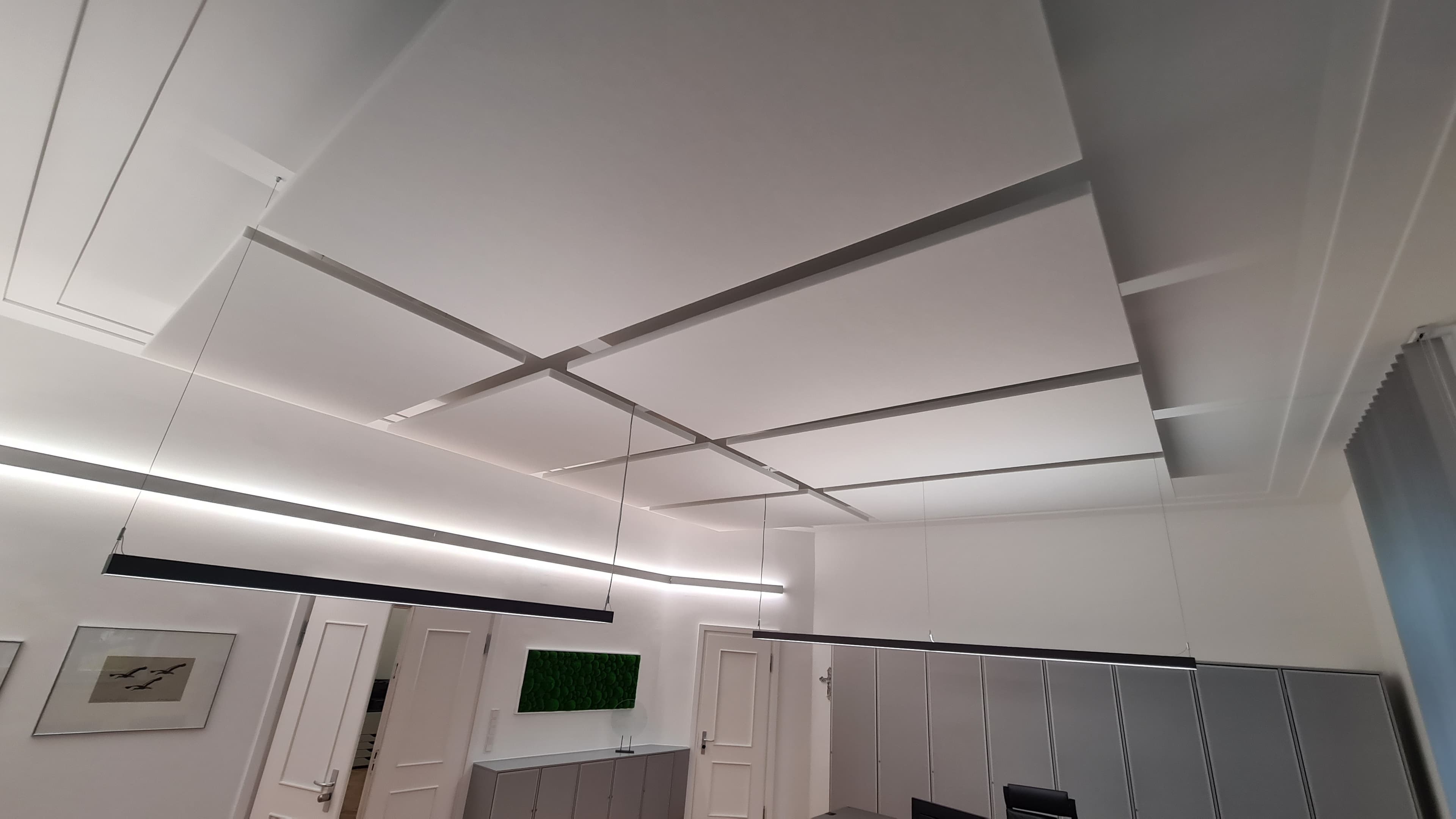 Raster aus weißen, rechteckigen Decken-Schallschutzelementen mit abgehängten LED-Linienleuchten.