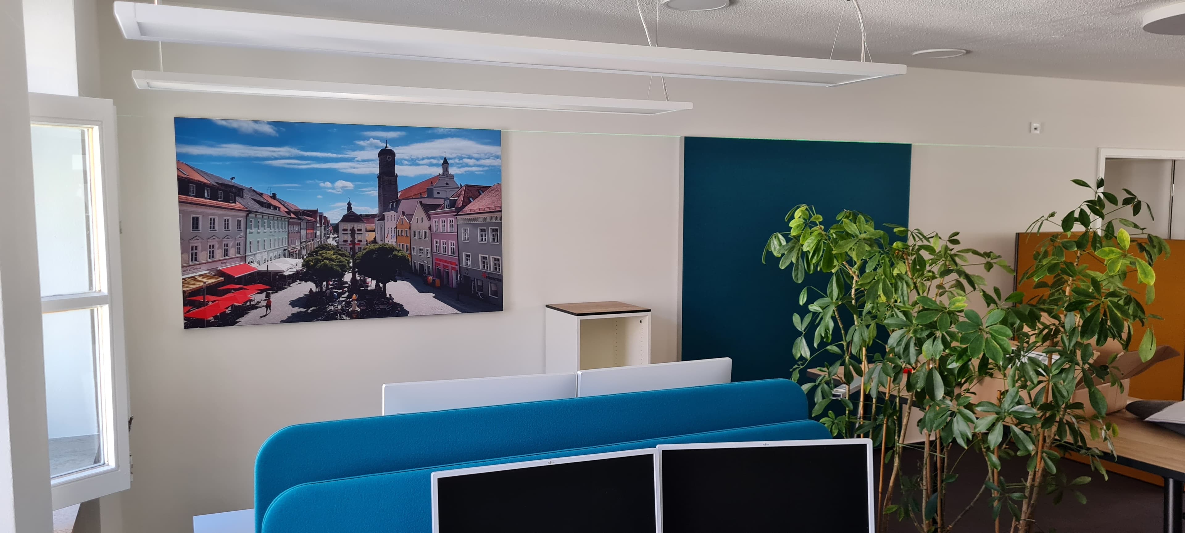 Büro mit weißen Deckenpaneelen sowie blauen Akustik-Trennwänden und einem Wandpaneel aus Merino-Stoff.